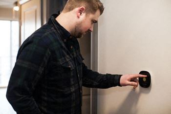 A man in a plaid shirt is pressing a round black button on a wall.